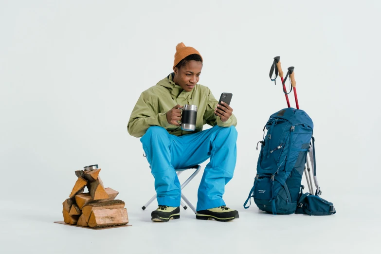 a man sitting on a chair looking at his cell phone, by Hamish MacDonald, hiking clothes, tyler the creator, wearing adventure gear, green and blue and warm theme