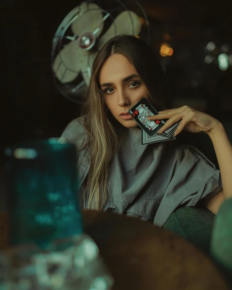 a woman sitting at a table with a cell phone in her hand, a polaroid photo, inspired by Elsa Bleda, pexels contest winner, surrealism, holding an ace card, soft devil queen madison beer, in a pub, underexposed grey