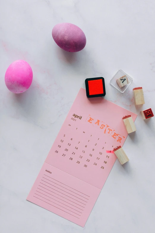 a calendar sitting on top of a table next to eggs, by Julia Pishtar, pexels contest winner, pink concrete, rubber stamp, with fluo colored details, thumbnail