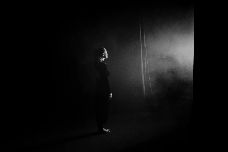 a person that is standing in the dark, a black and white photo, by Emma Andijewska, conceptual art, recital, kirsi salonen, dark. studio lighting, background ( dark _ smokiness )