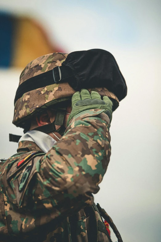 a man in camouflage holding a cell phone to his ear, a colorized photo, unsplash, holding helmet, plain uniform sky, facepalm, multicoloured