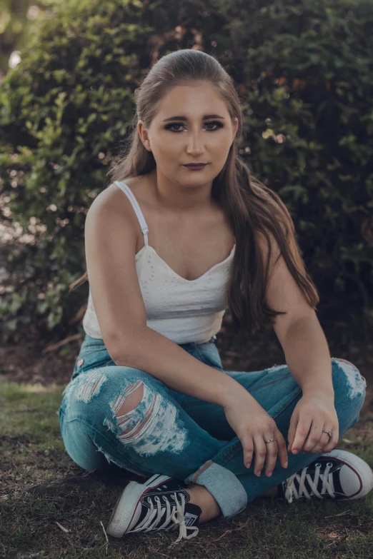 a woman sitting on the ground in front of a bush, inspired by Sydney Carline, pexels contest winner, ripped jeans, headshot profile picture, teenage, white and teal garment