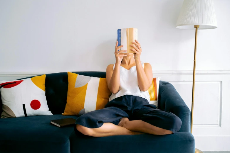 a woman sitting on a couch reading a book, inspired by Sarah Lucas, pexels contest winner, alexandria ocasio - cortez, surprising, slightly minimal, a wooden