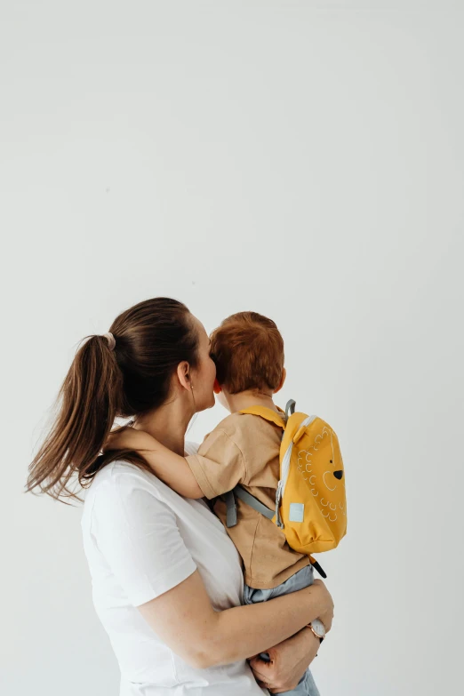 a woman holding a baby wearing a backpack, pexels contest winner, minimalism, yellow scheme, brunette boy and redhead boy, profile image, waist reaching ponytail