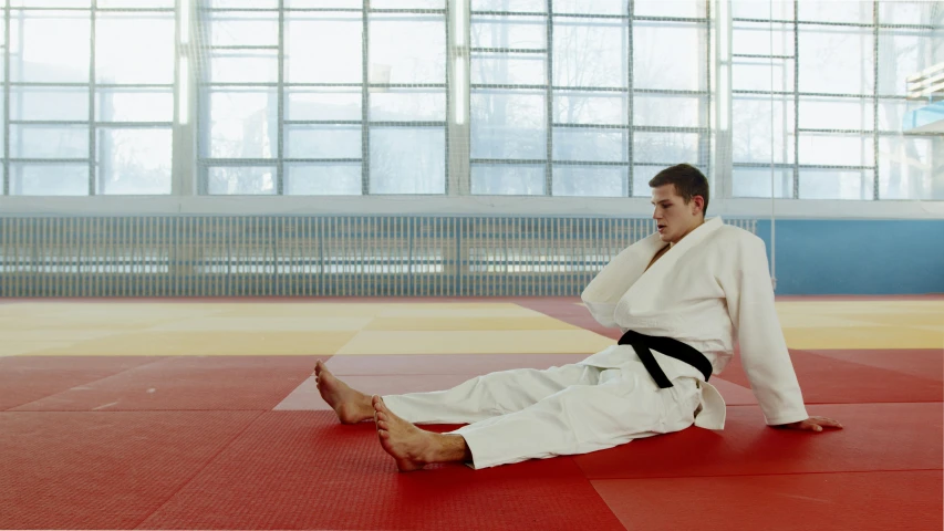 a man in a white kimono sitting on a red mat, a picture, unsplash, local gym, 2000s photo, fighting, getty images