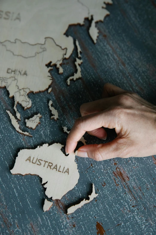 a person holding a piece of paper with the word australia on it, a jigsaw puzzle, trending on unsplash, globes, carved in wood, asian, mapbox