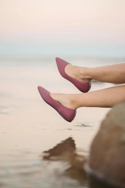 a woman is sitting on a rock in the water, pointy jester shoes, maroon red, smooth matte, flat colour-block style