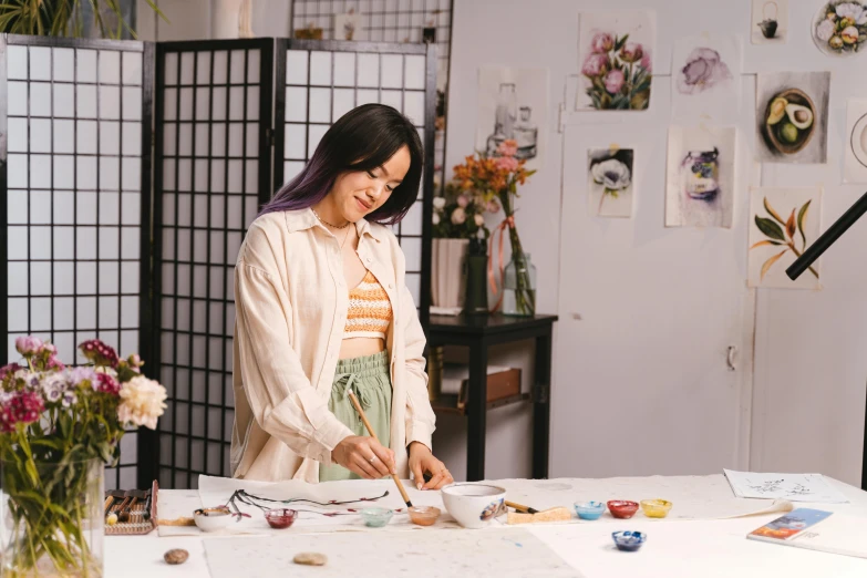 a woman that is standing in front of a table, a watercolor painting, inspired by helen huang, trending on pexels, process art, ceramics, japanese calligraphy, girl in studio, character designs painting