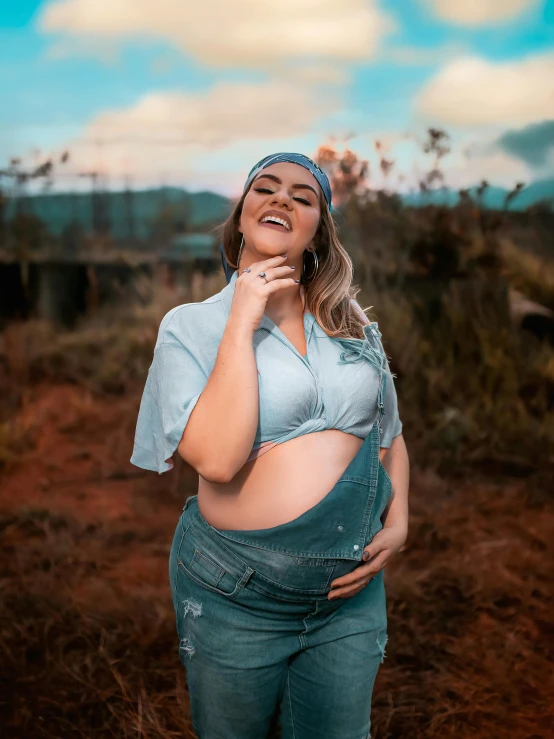 a pregnant woman standing in the middle of a field, an album cover, inspired by Elsa Bleda, pexels contest winner, happening, smiling laughing, brazilian, blue overalls, she has a jiggly fat round belly