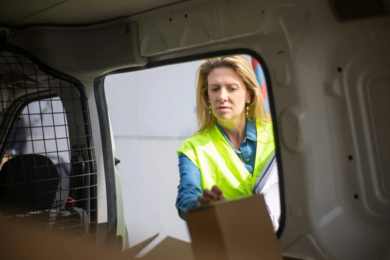 a woman in a safety vest looking out the window of a van, cardboard, ergonomic, avatar image, maintenance photo