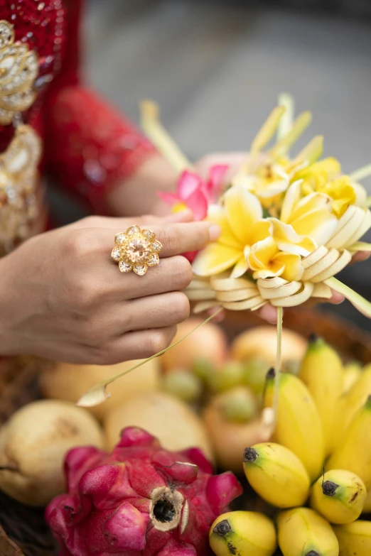 a close up of a person holding a basket of fruit, gold flowers, jakarta, rings, plumeria