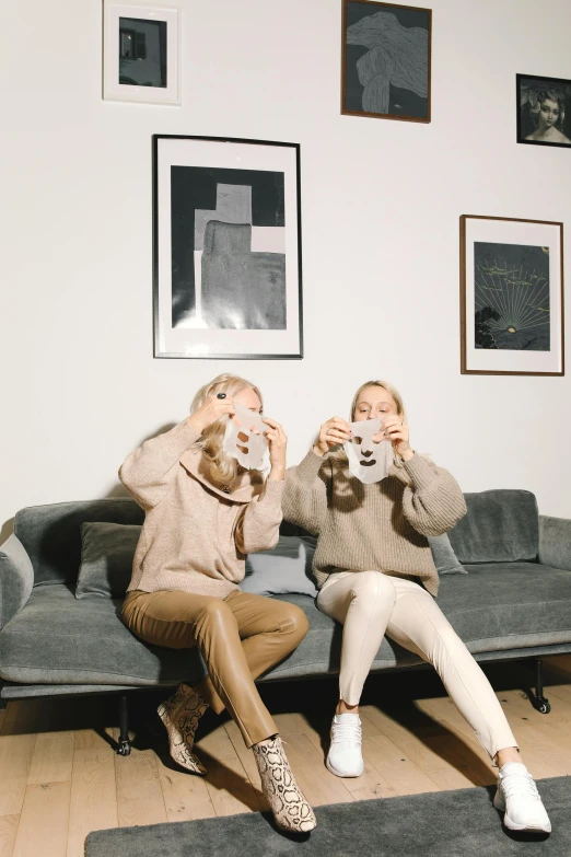 a couple of women sitting on top of a couch, by Nina Hamnett, trending on pexels, aestheticism, the mask covers her entire face, scandinavian design, wearing a sweater, instagram picture