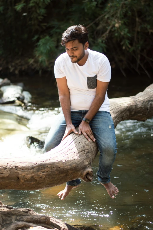 a man sitting on a log in a river, a picture, by Max Dauthendey, hurufiyya, jeans and t shirt, jayison devadas, forest setting, casually dressed