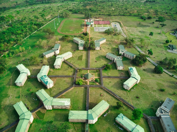 a group of buildings sitting on top of a lush green field, prison complex, neco arc, post graduate, uav