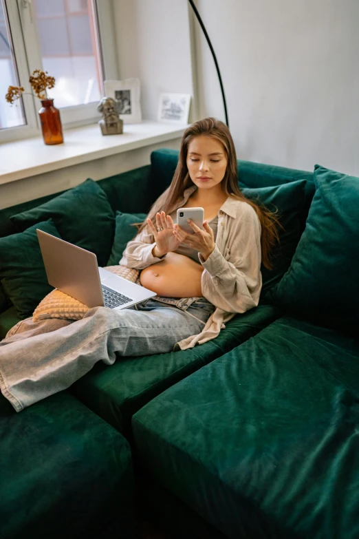 a woman sitting on a green couch using a laptop, by Adam Marczyński, trending on pexels, happening, pregnant belly, looking at his phone, portrait sophie mudd, ( 3 1