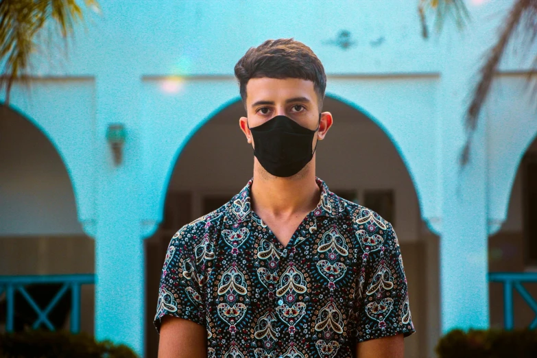 a man wearing a face mask standing in front of a building, an album cover, pexels contest winner, renaissance, young spanish man, middle eastern skin, youtuber, wearing a light blue shirt