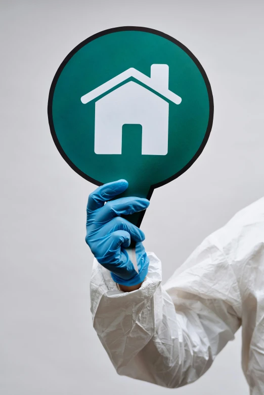 a man in a hazmat suit holding a house sign, by Derek Hill, shutterstock, plasticien, white and teal garment, press shot, mit technology review, round-cropped