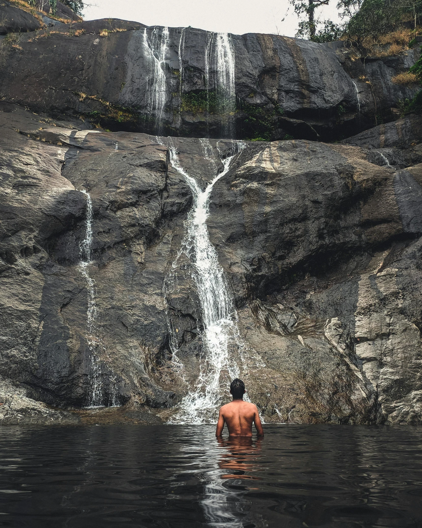 a man standing in the water in front of a waterfall, sri lankan landscape, lgbtq, swimming, multiple stories