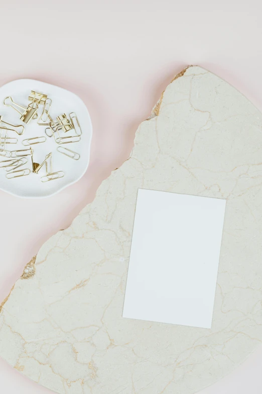 a piece of paper sitting on top of a table, by Nicolette Macnamara, trending on pexels, marble and hint gold, light pink background, white ceramic shapes, metal plate photograph