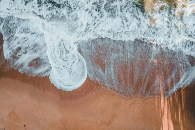 a person riding a surfboard on top of a sandy beach, pexels contest winner, swirling fluid, looking down from above, red sand beach, wall of water either side