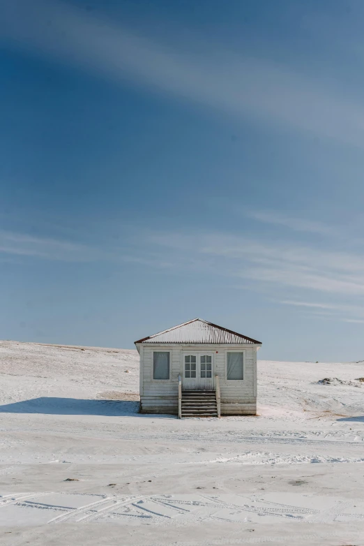 a small white house sitting on top of a snow covered field, unsplash contest winner, postminimalism, clear blue skies, near the seashore, old cabin, uniform off - white sky