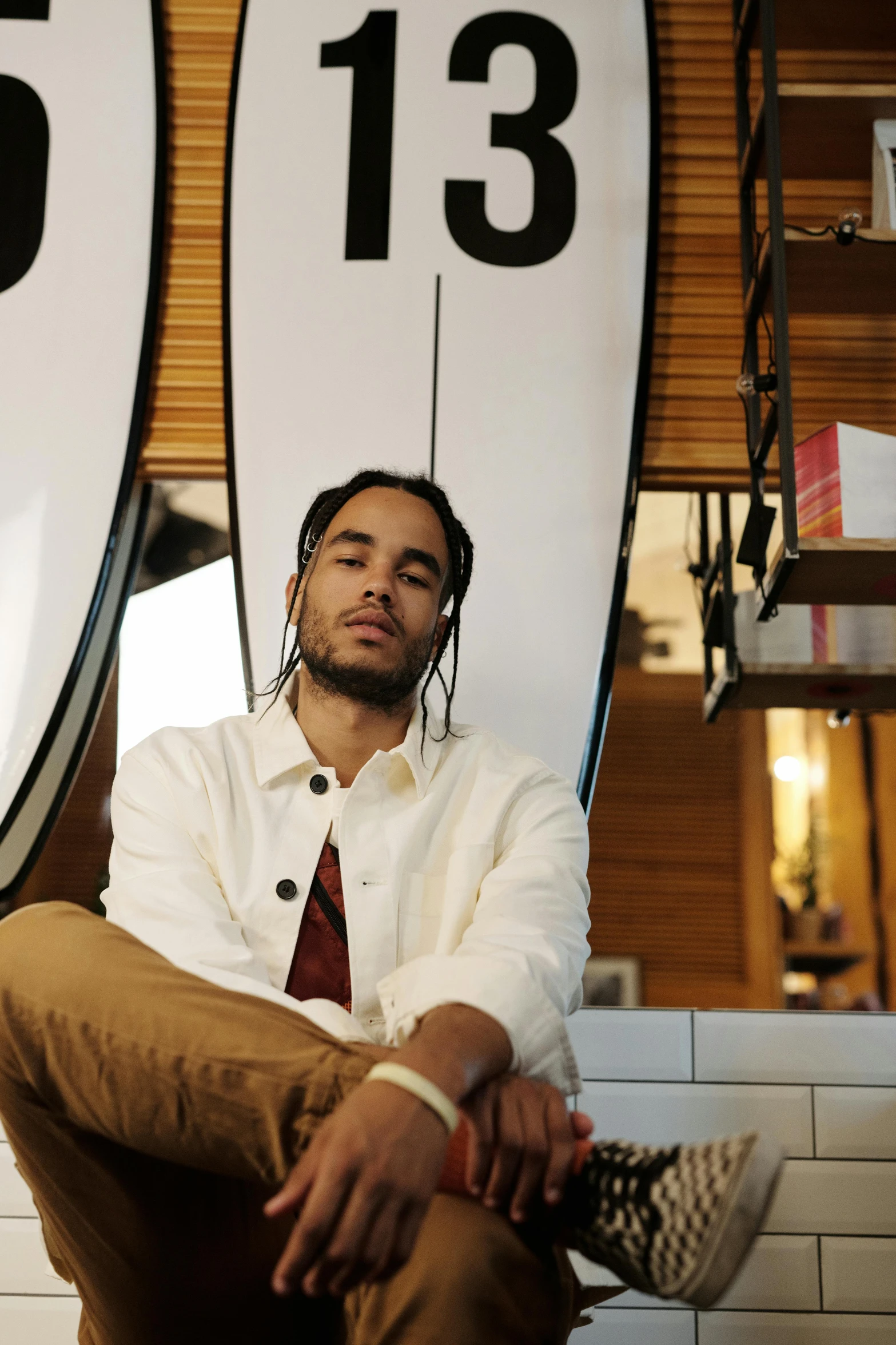 a man sitting in front of two surfboards, zoë kravitz, wearing a white button up shirt, in a coffee shop, portrait featured on unsplash