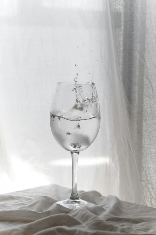 a glass of water sitting on top of a bed, by Matija Jama, pexels contest winner, photorealism, 🍸🍋, drops are falling from above, on a pale background, wining