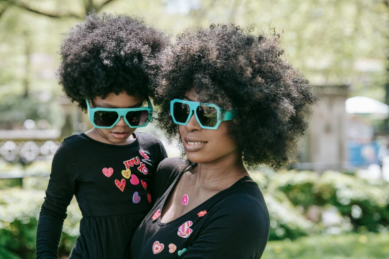 a woman standing next to a little girl wearing sunglasses, by Lily Delissa Joseph, pexels contest winner, afrofuturism, black and aqua colors, with afro, lush unkempt black hair, adult pair of twins