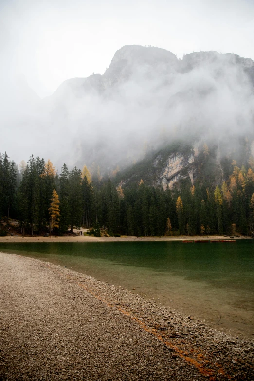 a body of water with a mountain in the background, by Luca Zontini, foggy forrest backdrop, dolomites, autum, sand mists