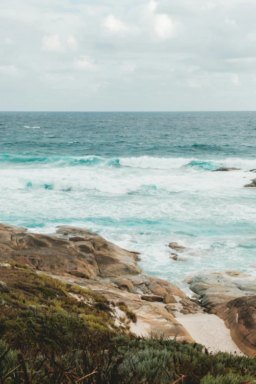 a man standing on top of a cliff next to the ocean, by Lee Loughridge, trending on unsplash, minimalism, waves crashing at rocks, an australian summer landscape, turquoise water, rhode island