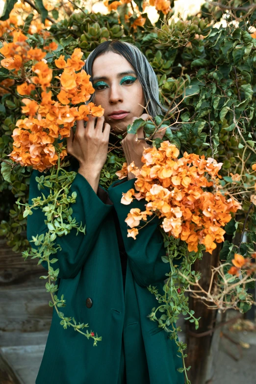 a woman holding a bunch of flowers in front of her face, a colorized photo, inspired by Elsa Bleda, trending on unsplash, orange jacket, arab inspired, branches and ivy, green clothes