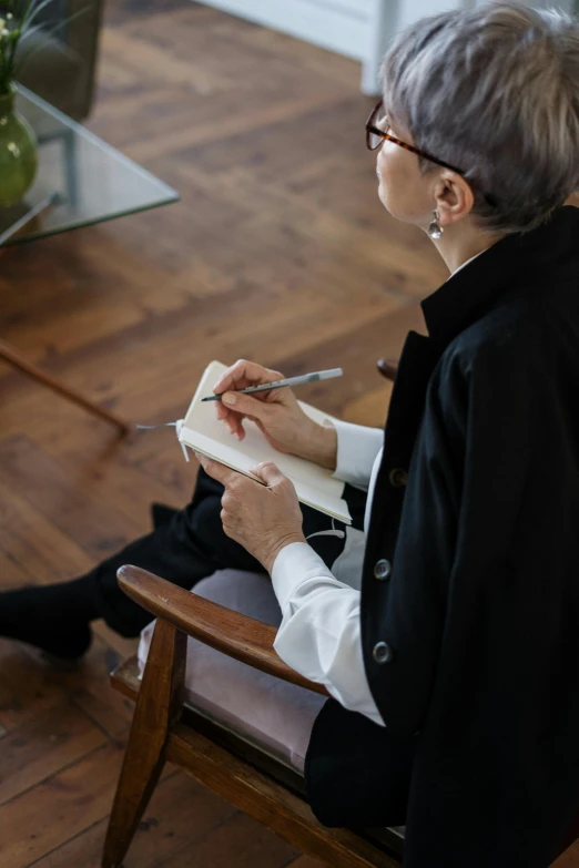 a woman sitting in a chair next to a cat, by Lucette Barker, trending on unsplash, visual art, holding pencil, ryuichi sakamoto, writing on a clipboard, older woman