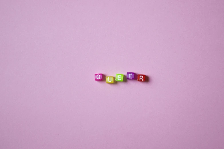 a couple of cubes that are sitting on top of a table, trending on pexels, feminist art, rainbow accents, letters, queen, pink