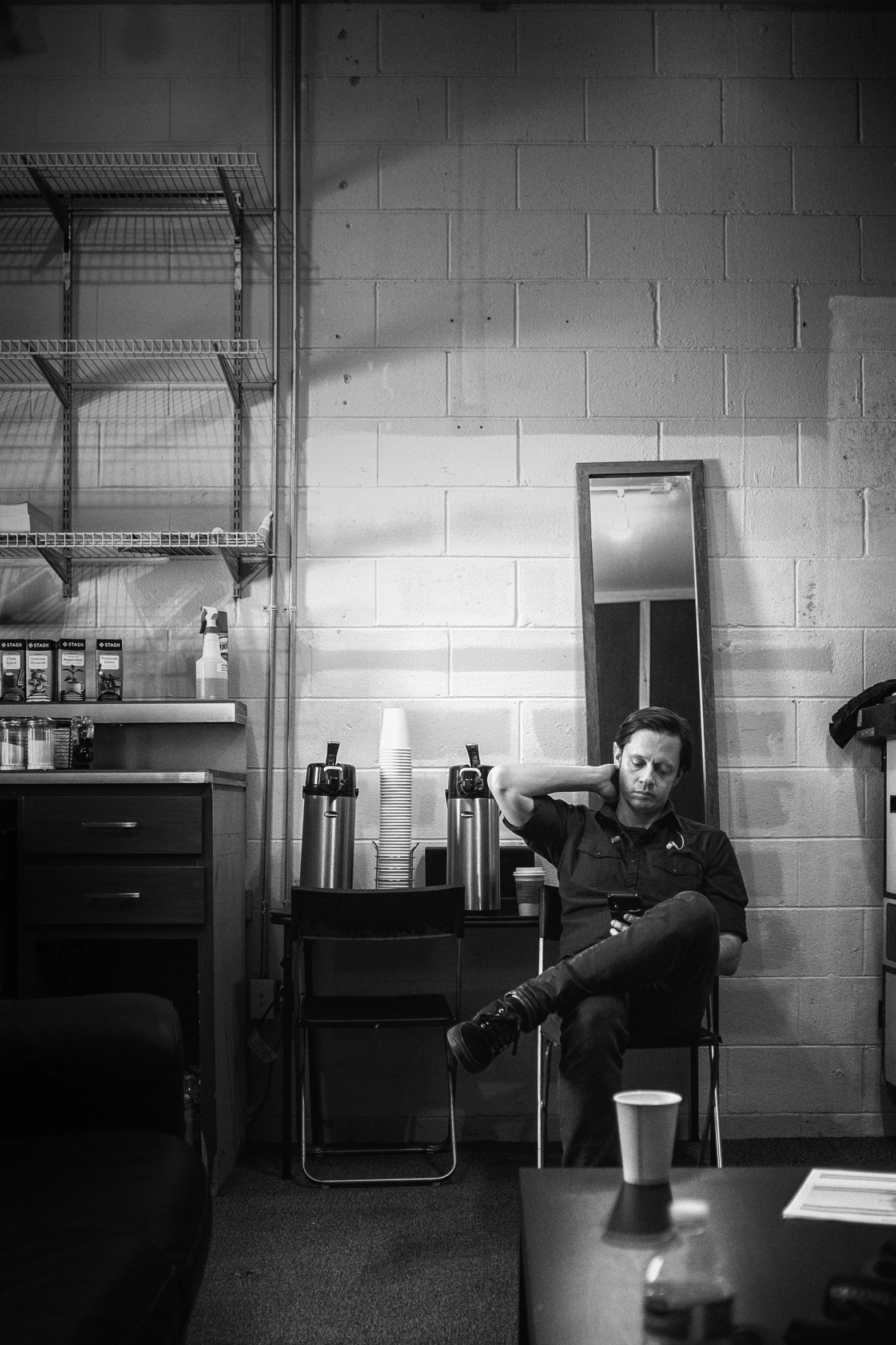 a man sitting in a chair in a room, a black and white photo, by Kevin Connor, pexels contest winner, aussie baristas, jeremy renner, she is in the potions workshop, location [ chicago ( alley ) ]