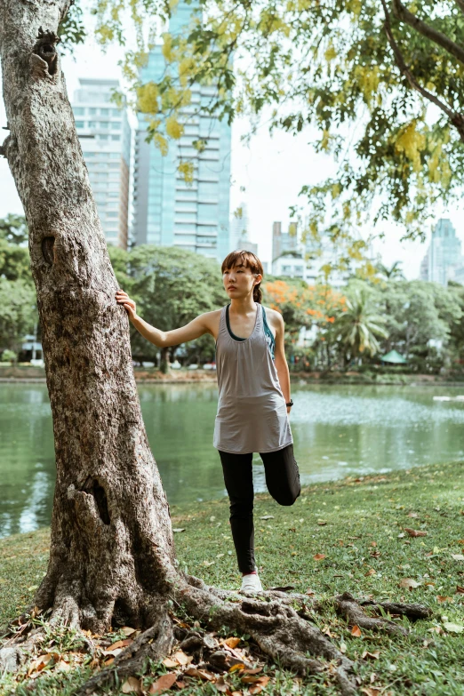 a woman standing next to a tree in a park, inspired by Ni Yuanlu, unsplash, happening, wearing fitness gear, bangkok, near pond, parkour
