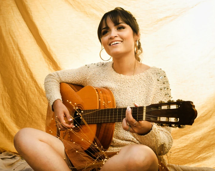 a woman sitting on the ground playing a guitar, an album cover, inspired by Glòria Muñoz, pexels contest winner, dau-al-set, ana de la reguera portrait, shiny gold, boke, lucy hale