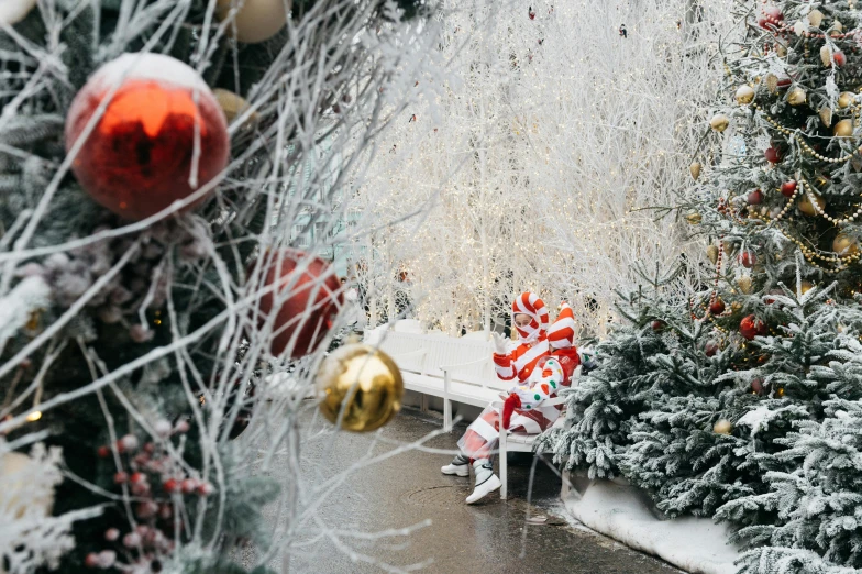 a person sitting on a bench in front of a christmas tree, pexels contest winner, where's waldo, against a winter garden, silver white red details, frozen and covered in ice