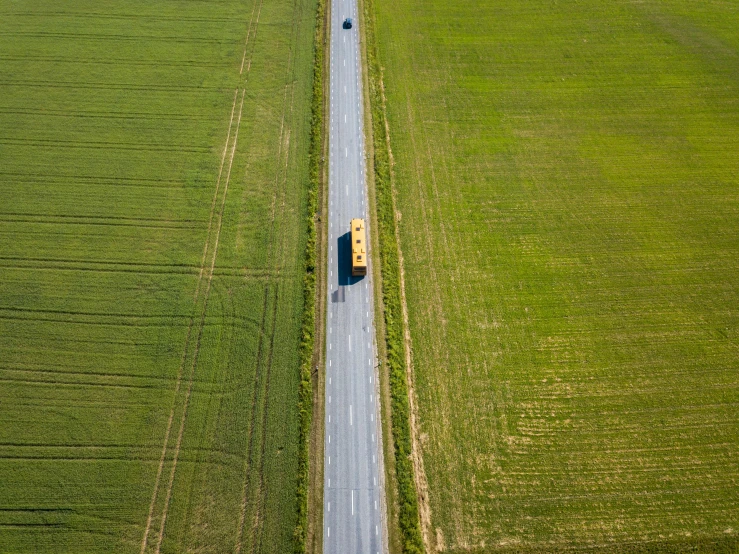 a yellow school bus driving down a country road, a picture, by Andries Stock, pexels contest winner, wide aerial shot, green fields, cardboard, maintenance photo