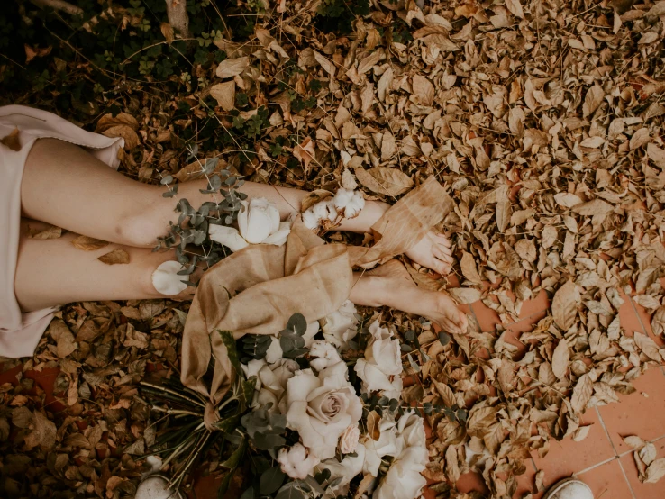 a person standing on top of a pile of leaves, by Jessie Alexandra Dick, pexels contest winner, aestheticism, laying on roses, earthy tones, bones lying on the ground, eucalyptus