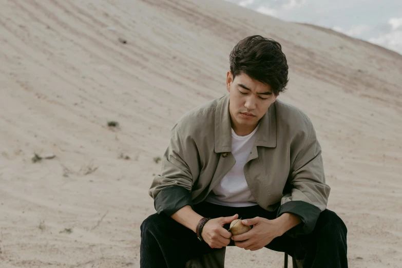 a man sitting on a skateboard in the sand, inspired by Zhang Han, trending on pexels, realism, looking at his phone, standing in a desert, declan mckenna, asian descent