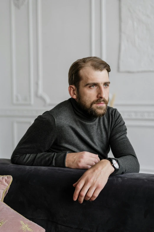 a man sitting on a couch in a living room, inspired by Serhii Vasylkivsky, trending on reddit, short dark blond beard, professional profile photo, wearing turtleneck, adult man