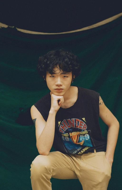 a young man sitting on top of a skateboard, an album cover, inspired by Yanjun Cheng, realism, (dark shorter curly hair), wearing a tanktop, detailed face of a asian boy, androgynous male