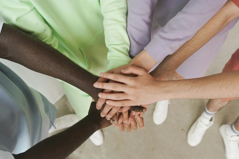 a group of people putting their hands together, a colorized photo, trending on pexels, antipodeans, green and purple, skin color, arms crossed, an all white human