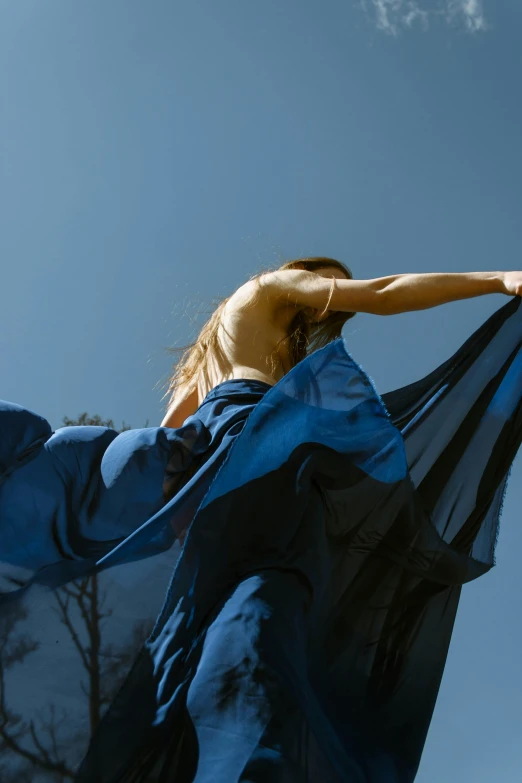 a woman in a blue dress is flying a kite, an album cover, by Maciej Kuciara, unsplash, arabesque, large draped cloth, on a sunny day, contemporary dance, indigo