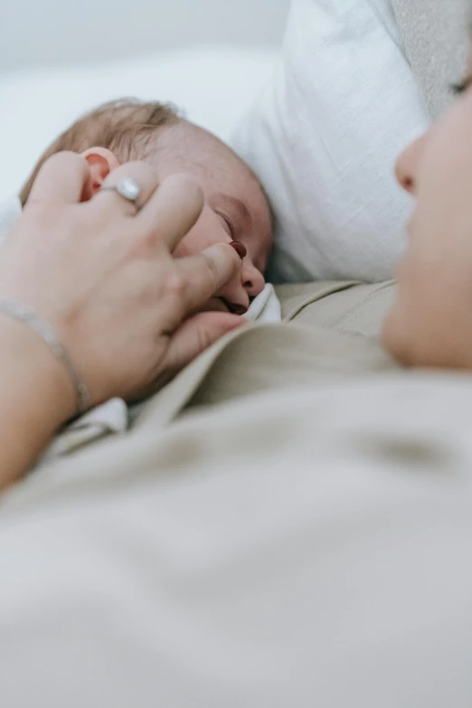 a woman laying on top of a bed next to a baby, by Carey Morris, pexels, symbolism, hand on his cheek, comforting, ignant, detail shot