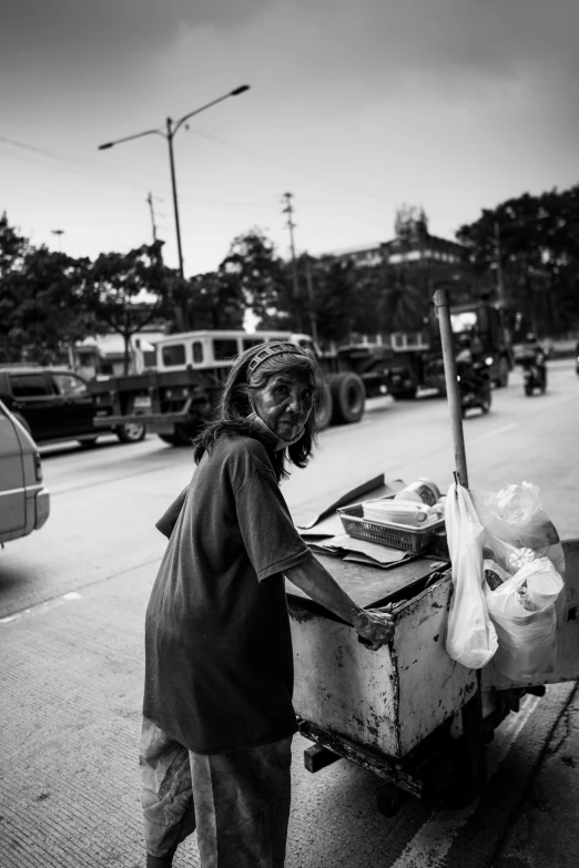 a man pushing a cart down a street, a black and white photo, by Andrew Stevovich, pexels contest winner, auto-destructive art, at the counter, photo of a woman, manila, trailer-trash lifestyle