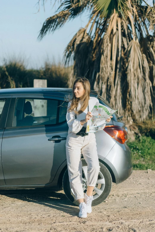 a woman standing next to a car on a dirt road, reading a newspaper, octane renter, grey, promo image