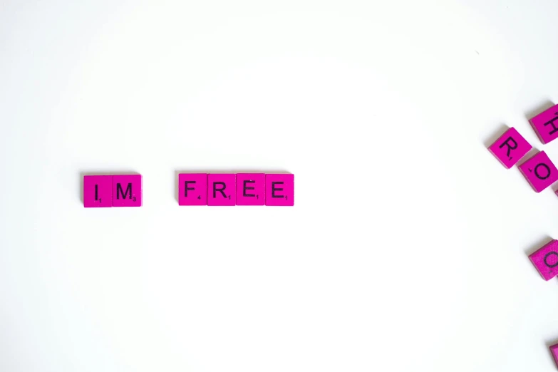 pink scrabbles spelling i'm free on a white surface, a photo, pexels, minimalism, frameless, streamlined pink armor, ad image, skin