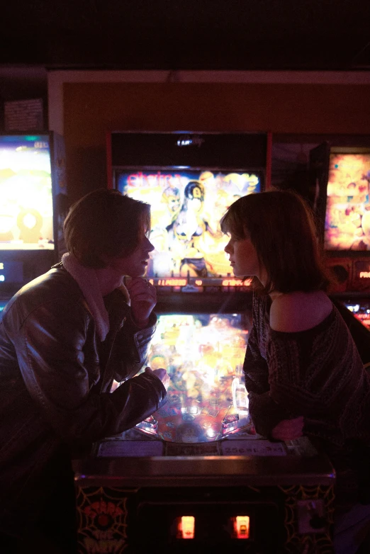 a couple of people playing a game of pinball, poster art, inspired by Nan Goldin, pexels, emma stone in stranger things, sitting alone at a bar, undertale, facing each other