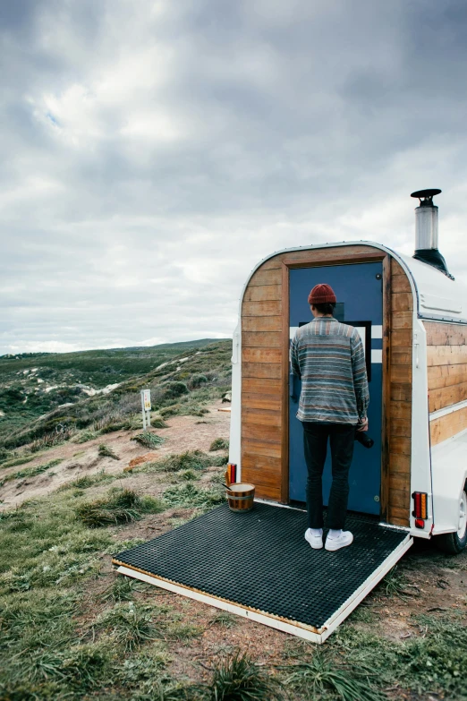 a man standing in the doorway of a tiny trailer, trending on unsplash, happening, woodfired, seaview, built on a steep hill, whealan